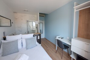 Quarto de hotel moderno com cama, mesa de cabeceira, escrivaninha, cadeira e um espelho grande.