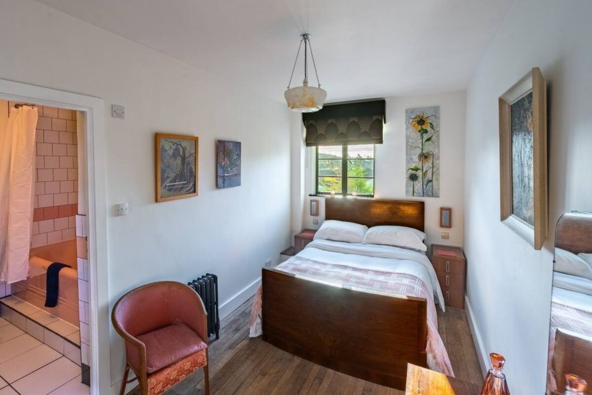 A bedroom with a wooden bed, a chair, a radiator, and artwork on the walls.