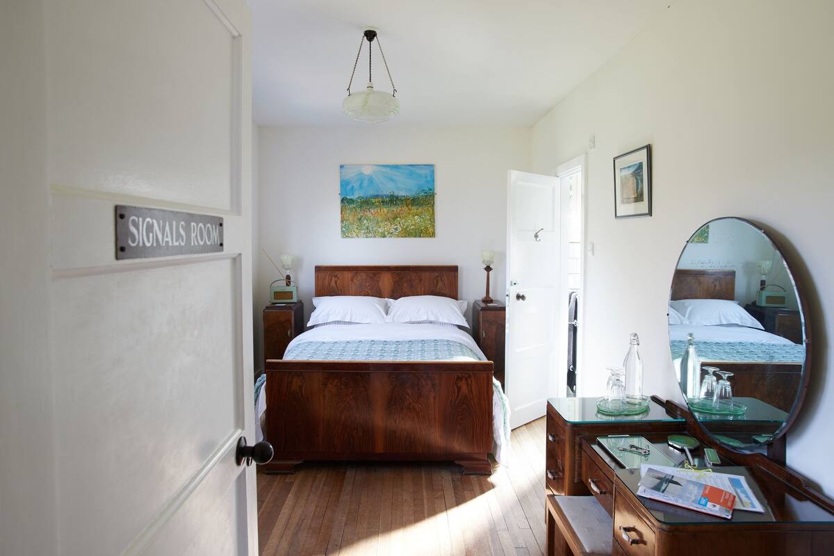 A bedroom with a wooden bed, a bedside table with a lamp, a dresser, and a mirror.