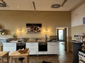 A modern kitchen with white cabinets, a central island, and a coffee station. - Hotel an der Burg (Wettenberg)
