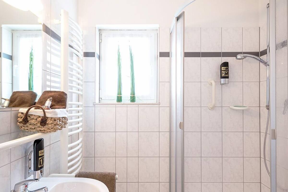 Ein Badezimmer mit einem weißen Waschbecken, einer Duschkabine aus Glas und einem Fenster mit Grünpflanzen.