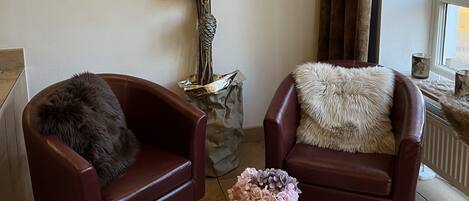 A room with two leather armchairs, a small wooden table with a bowl of decorative items, and a wall-mounted light fixture.
