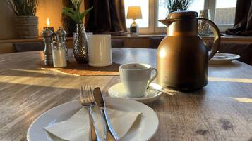 Una mesa dispuesta con un plato, cubiertos, una taza y una cafetera.