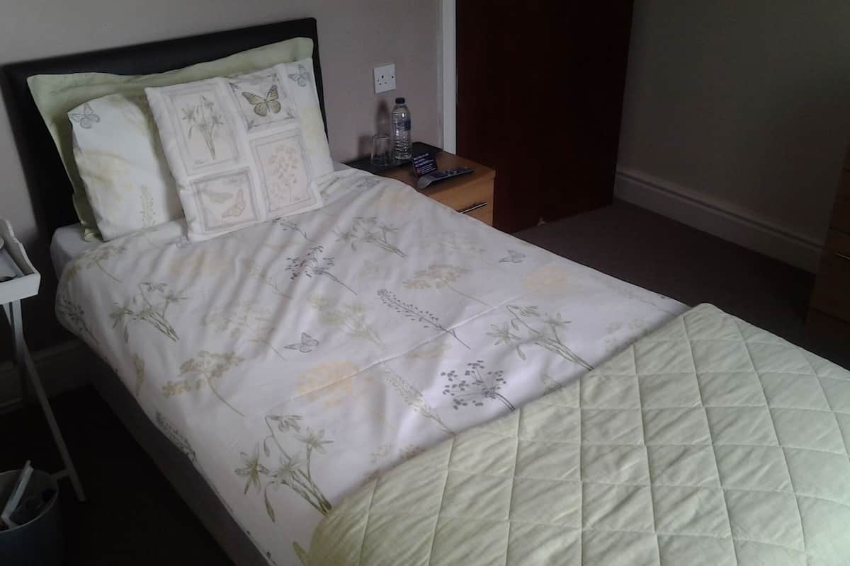 Una cama bien hecha con ropa de cama floral y un cubrecolchón acolchado. Hay una mesita de noche con una botella de agua y un vaso junto a la cama.