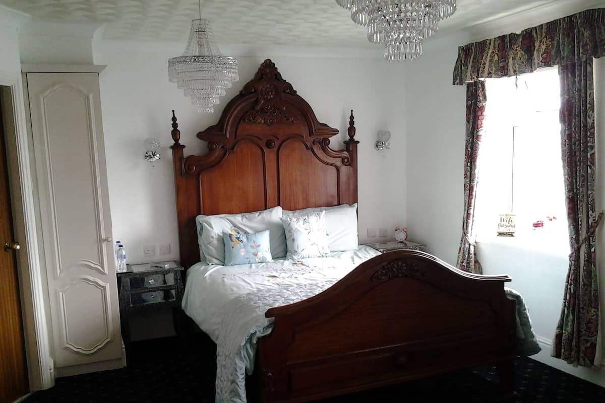 Un dormitorio con cama de madera, mesita de noche, candelabro y ventana con cortinas.