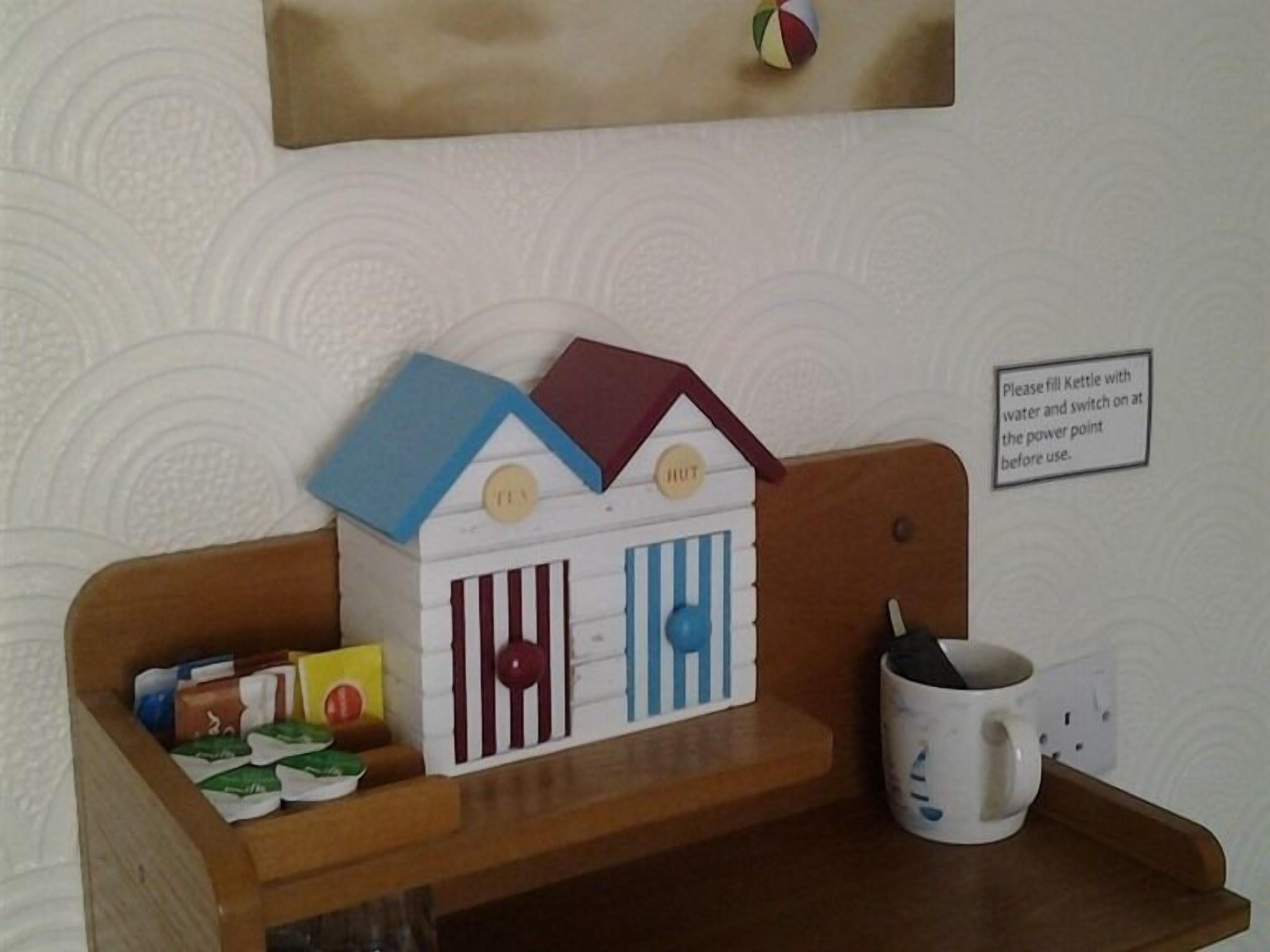 Ein kleines Holzregal mit einem Spielzeughaus, einem Wasserkocher und verpackten Snacks.