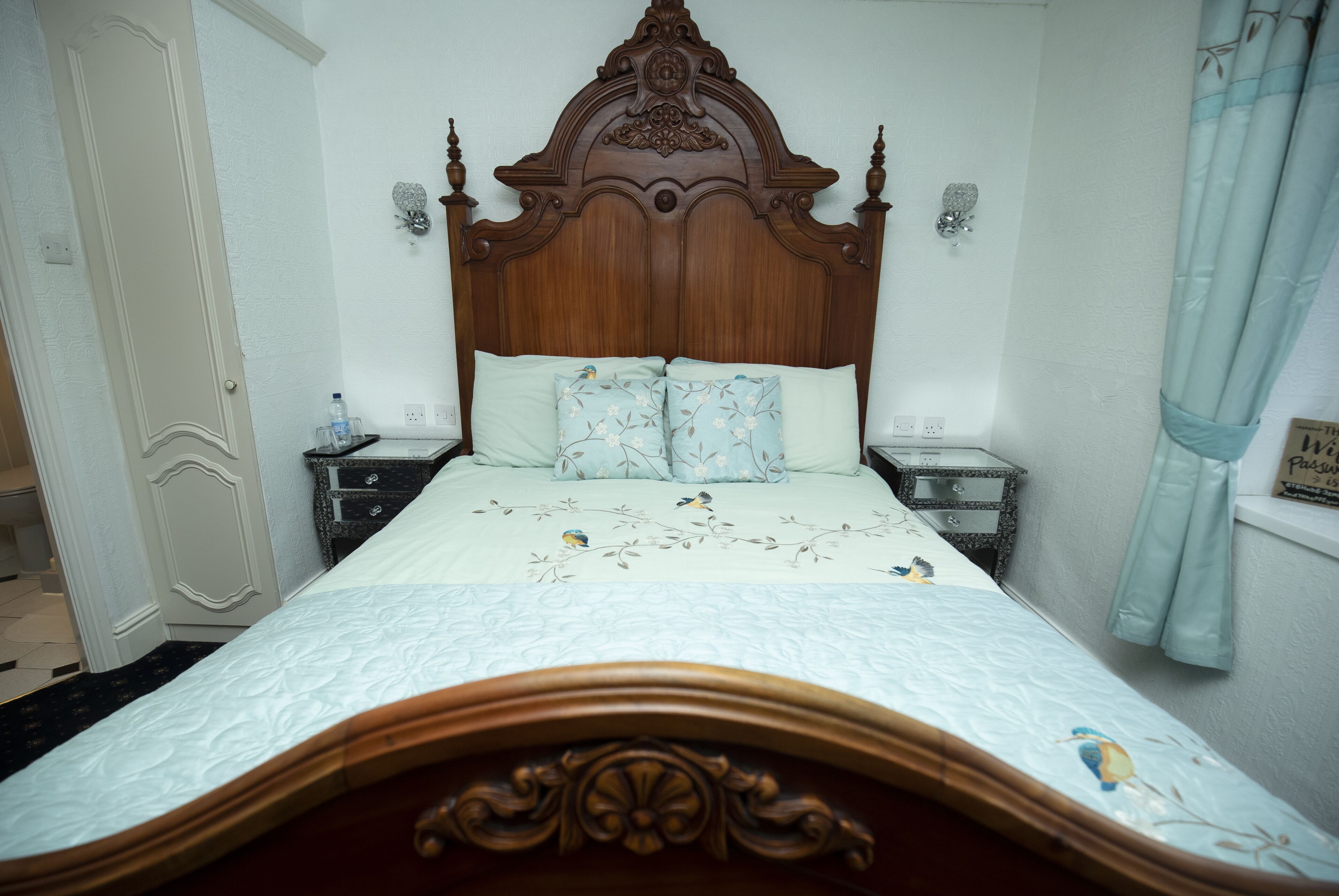 A bedroom with a wooden headboard, a bed with floral bedding, two bedside tables, and a nightstand with a lamp.