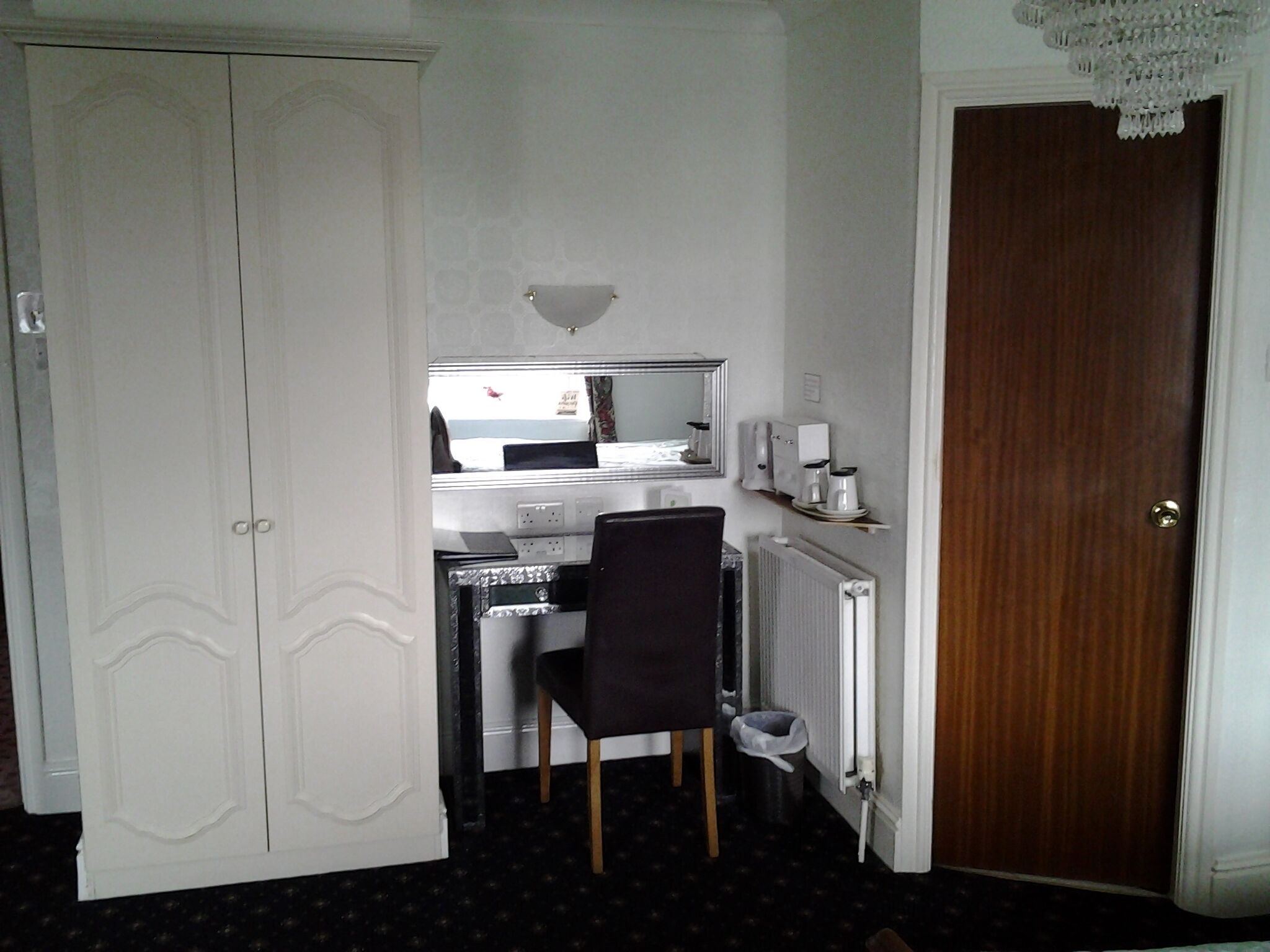 Ein kleines Hotelzimmer mit einem Einzelbett, einem Schreibtisch mit Stuhl, einem Heizkörper und einem Kleiderschrank.