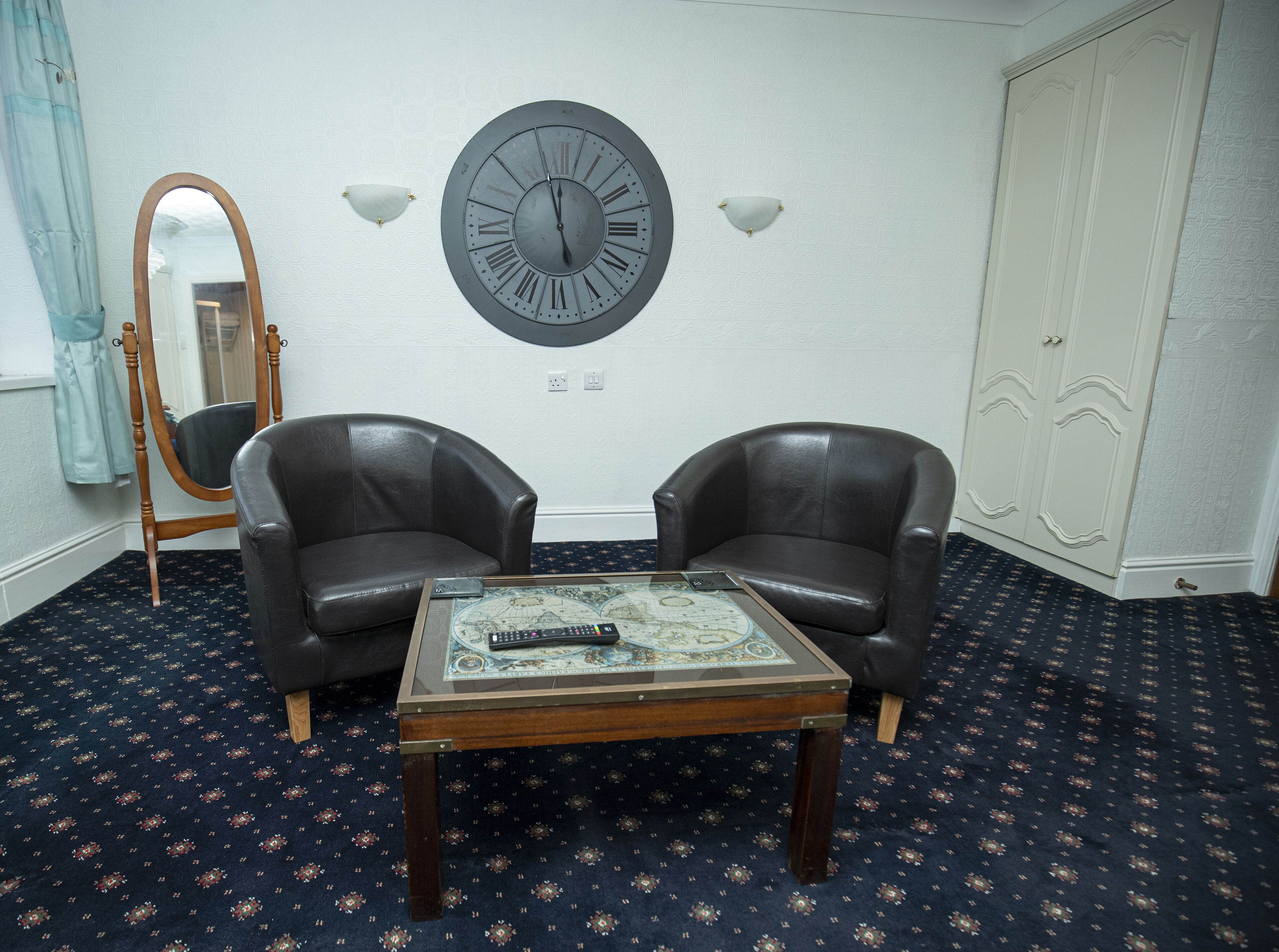 Ein Zimmer mit zwei Ledersesseln, einer runden Wanduhr, einem Spiegel und einem Tisch mit einer dekorativen Karte.
