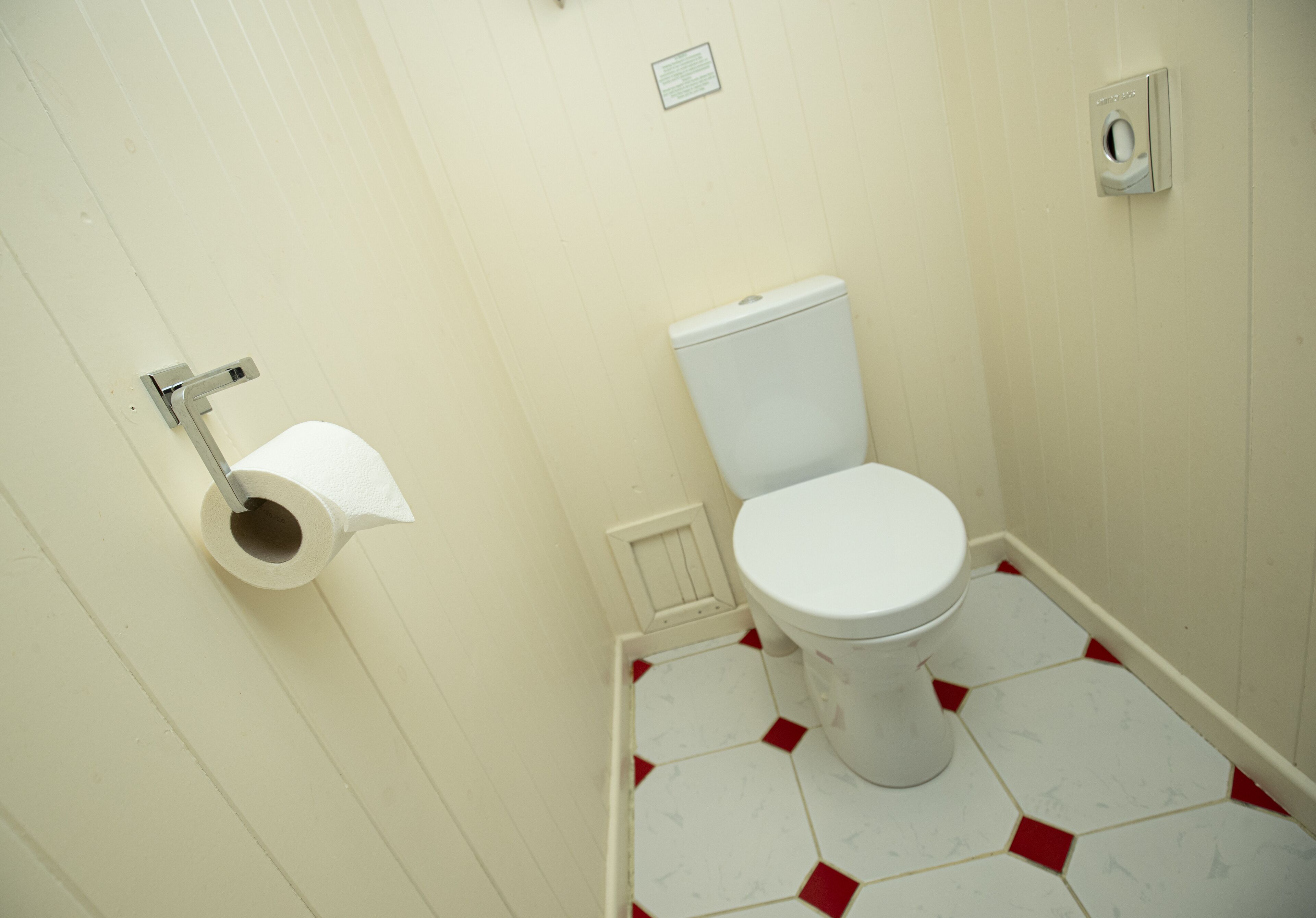 A small bathroom with a toilet, a toilet paper holder, and a tiled floor.