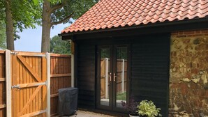 A patio area with a wooden fence, a covered grill, and potted plants.