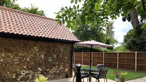 A backyard patio with a brick wall, a stone chimney, a table with chairs, and a wooden fence.