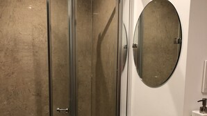 A modern bathroom with a glass-enclosed shower, a white sink, and a round mirror.