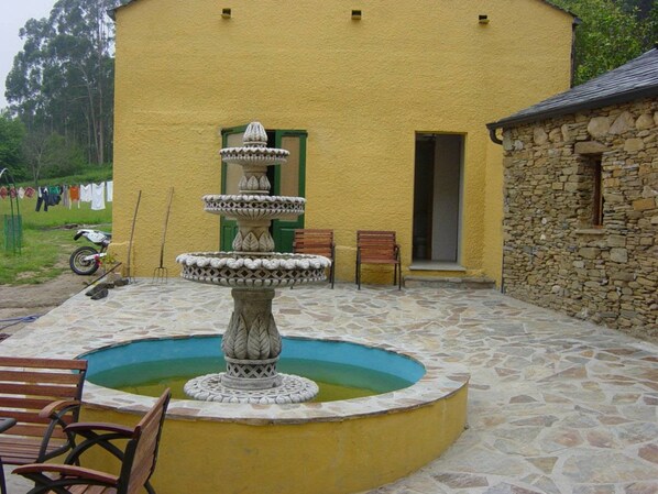 A stone fountain with a tiered design in front of a yellow building.