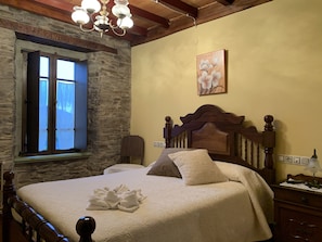Un dormitorio con pared de piedra, estructura de cama de madera, candelabro y un cuadro en la pared.