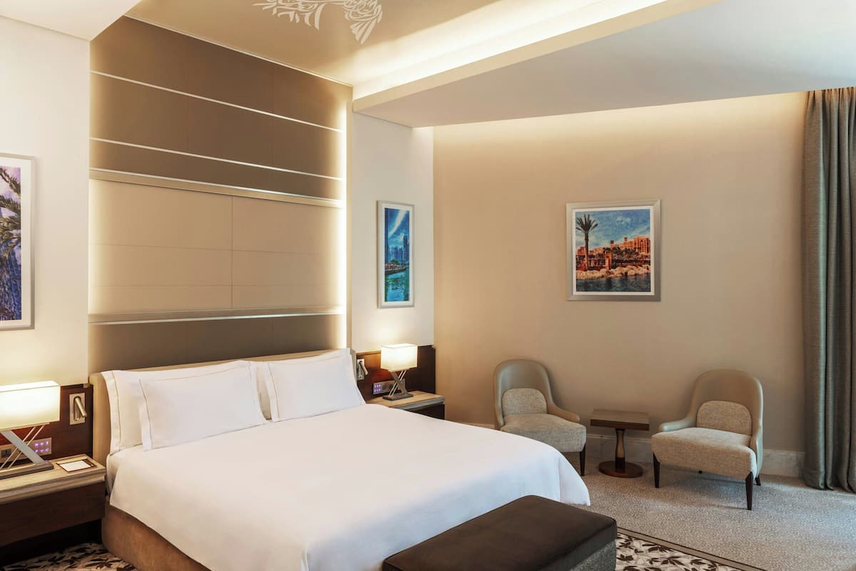 Ein Hotelzimmer mit einem großen Bett, zwei Sesseln, einem kleinen Tisch und Bildern an den Wänden.