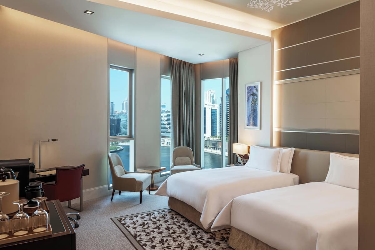 Ein Hotelzimmer mit einem großen Bett, einem Schreibtisch, einem Sessel und Blick auf die Stadt.