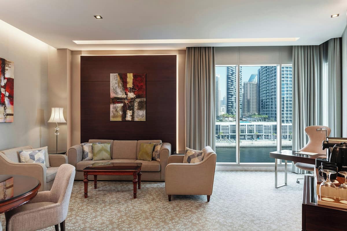Ein modernes Hotelzimmer mit großem Fenster und Blick auf die Stadt, einer Sitzecke, einer Kaffeestation und einem dekorativen abstrakten Gemälde an der Wand.