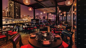 Un restaurante con mesas redondas, sillas acolchadas rojas y lámparas colgantes.