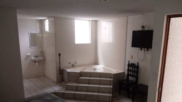 A bedroom with a bed, a bathroom with a sink, a bathtub, and a chair. - Hotel El 2000 (Morelia)
