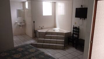 Un dormitorio con cama, un baño con lavamanos, bañera y una silla.