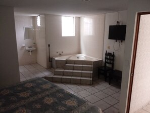 A bedroom with a bed, a bathroom with a sink, a bathtub, and a chair. - Hotel El 2000 (Morelia)