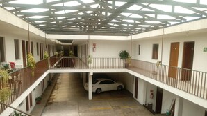 A multi-level parking area with a white car and a black car parked. There are potted plants along the railings and a fire extinguisher mounted on the wall. - Hotel El 2000 (Morelia)