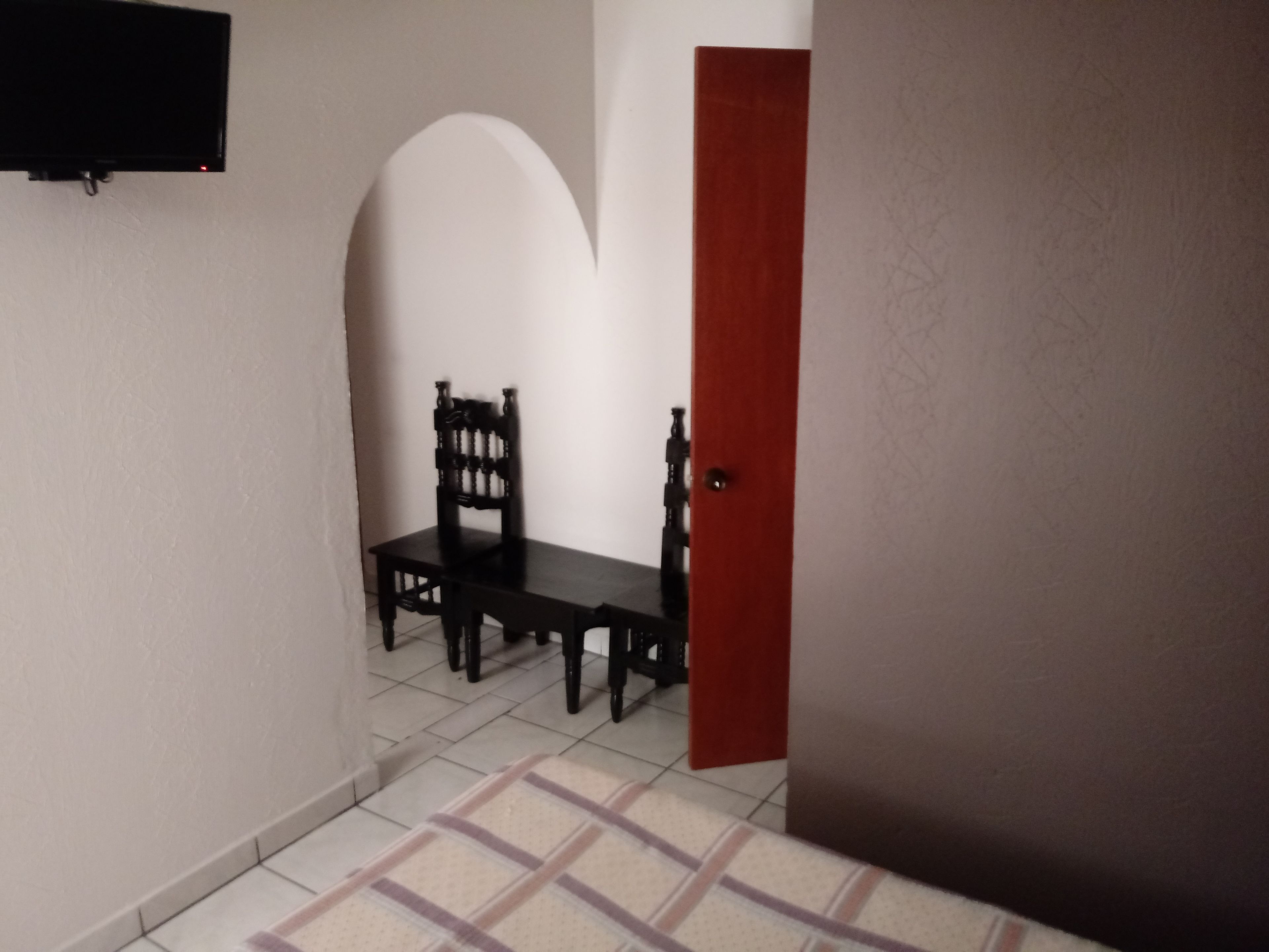 Un pasillo estrecho con suelo de baldosas, una silla de madera, una mesita y una puerta roja.