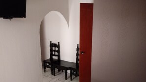 A narrow hallway with a tiled floor, a wooden chair, a small table, and a red door. - Hotel El 2000 (Morelia)