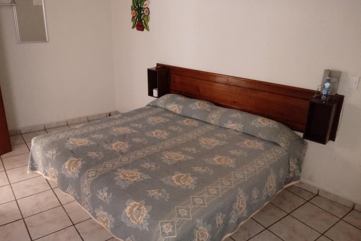 Un dormitorio con una cama, cabecera de madera, estante con una botella y decoración en la pared.
