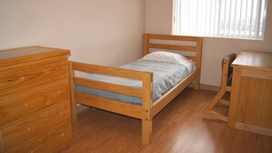 Una habitación pequeña con cama individual, muebles de madera, incluyendo un aparador y un escritorio.