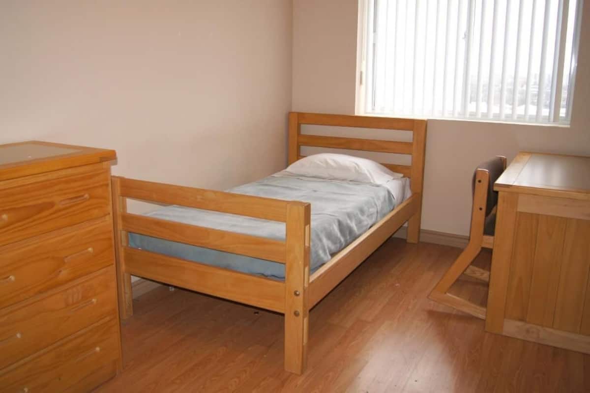 Quarto pequeno com uma cama de solteiro e móveis de madeira, incluindo uma cômoda e uma escrivaninha.
