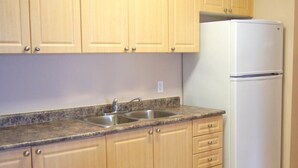 Una cocina con armarios de madera, encimera de granito, pileta doble y refrigerador blanco.