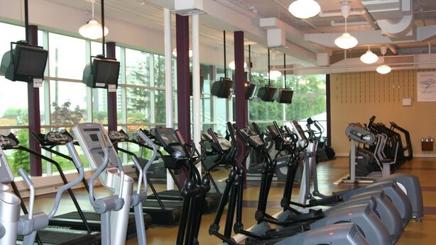 Un gimnasio con varias cintas de correr y bicicletas estáticas, ventanas amplias y equipamiento de ejercicio.