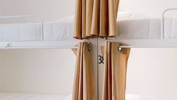 Quarto com beliches, cortinas, roupa de cama branca e compartimentos de armazenamento numerados.