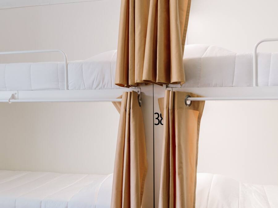 Habitación con literas, cortinas, ropa de cama blanca y compartimentos de almacenamiento numerados.