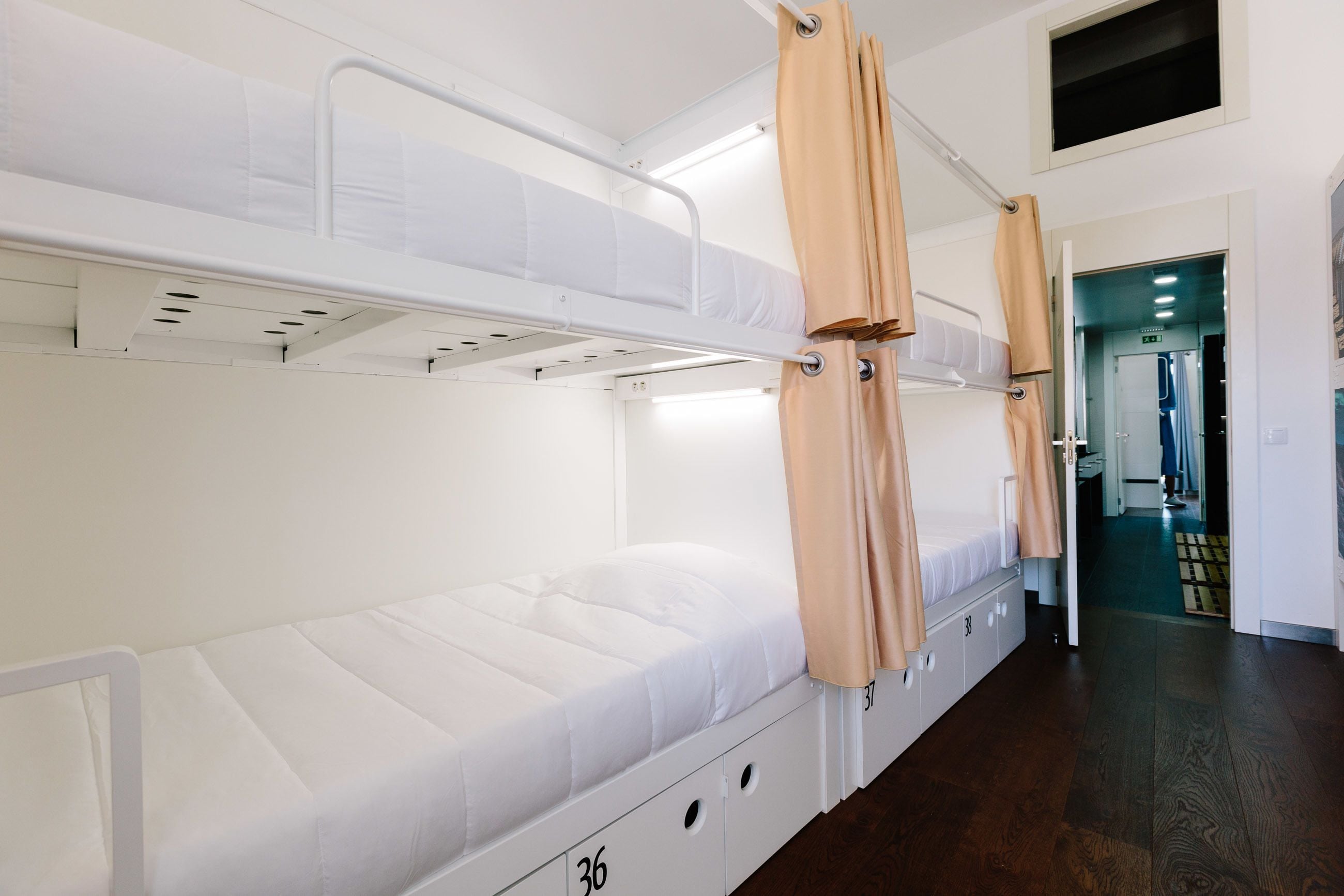A bunk bed room with a white mattress, beige curtains, and a wooden floor.