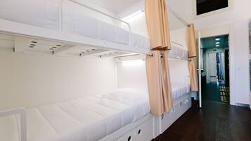 A bunk bed room with a white mattress, beige curtains, and a wooden floor.