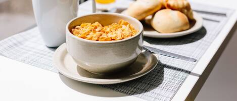 A breakfast table with a bowl of cereal, a glass of orange juice, a plate with croissants, and a cup.