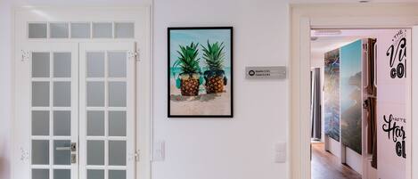 A hallway with a white door, a framed picture of pineapples on the wall, and a sign indicating room numbers.