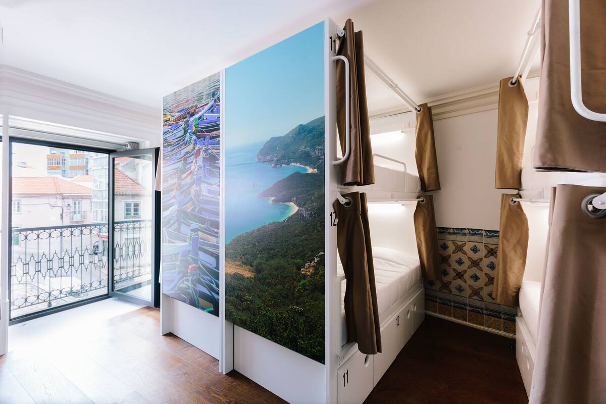 A balcony with a view of a coastal landscape, a white bed with brown curtains, and a tiled wall with a decorative pattern.