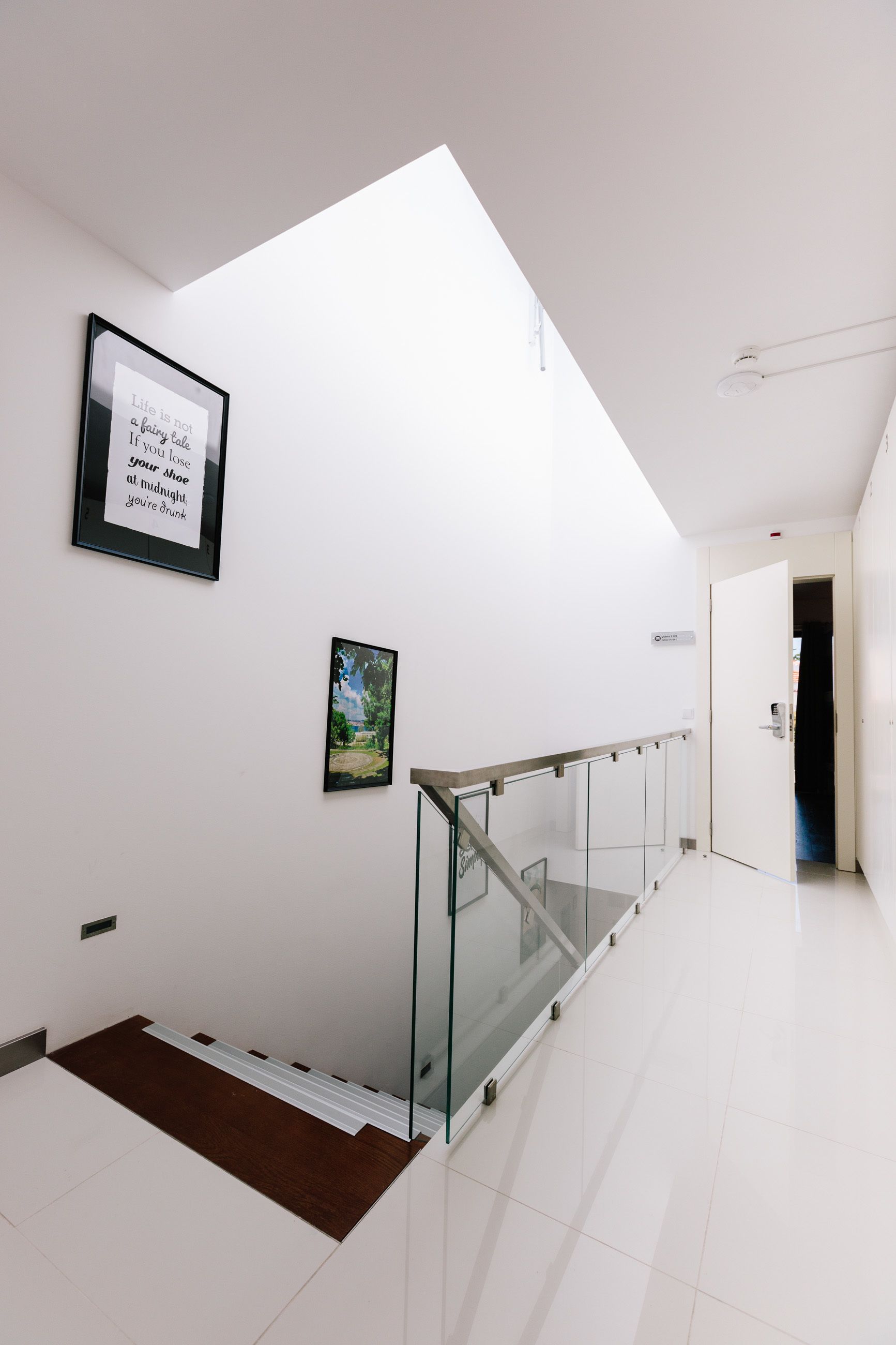 Un interior moderno con barandilla de vidrio, una cita enmarcada en la pared y vistas a una puerta que da a otra habitación.