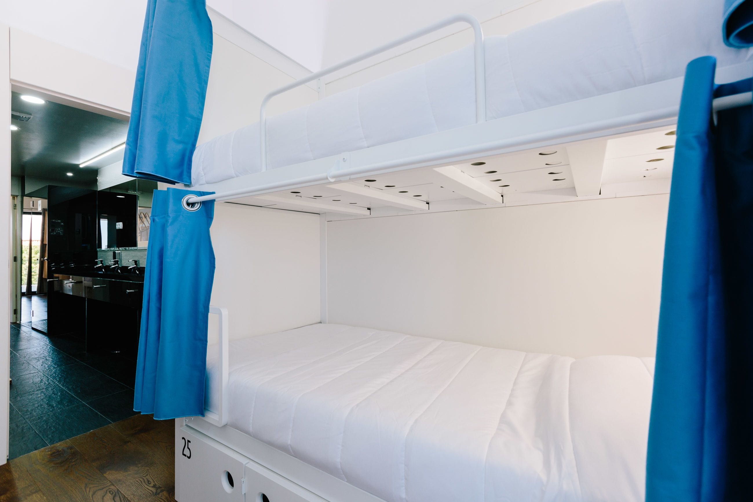 A bunk bed with a white mattress and blue curtains, a small drawer, and a number '25' on the side.
