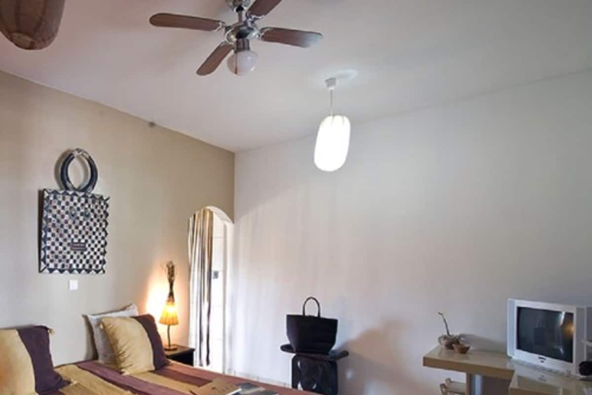 A bedroom with a bed, a desk with a computer, a ceiling fan, and a wall-mounted lamp.