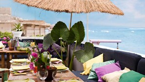 A dining table set with plates, glasses, and a vase of flowers, overlooking the sea.