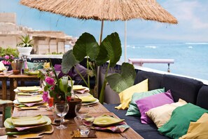 A dining table set with plates, glasses, and a vase of flowers, overlooking the sea. - Maison Abaka (Dakar)