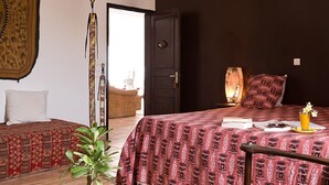 Una habitación con cama, una mesita, una planta y una puerta que da a otra estancia.