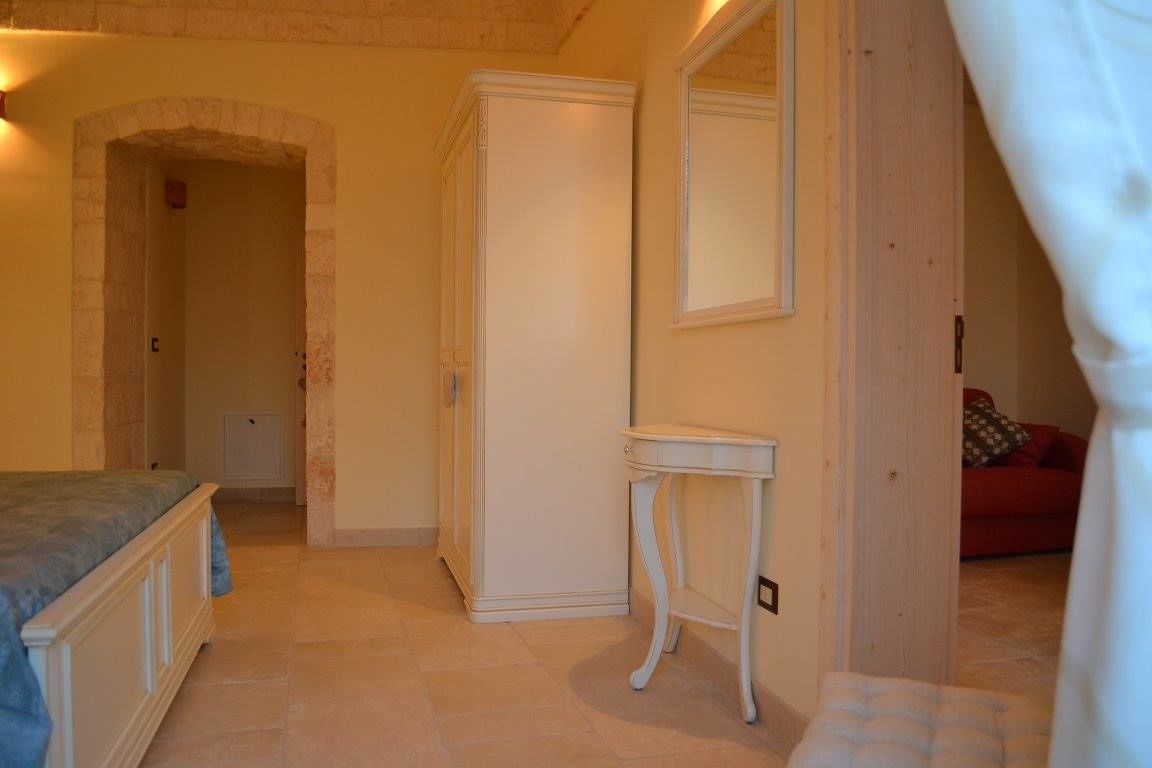 Une chambre à coucher avec un lit, une armoire, une petite table et un miroir au mur.