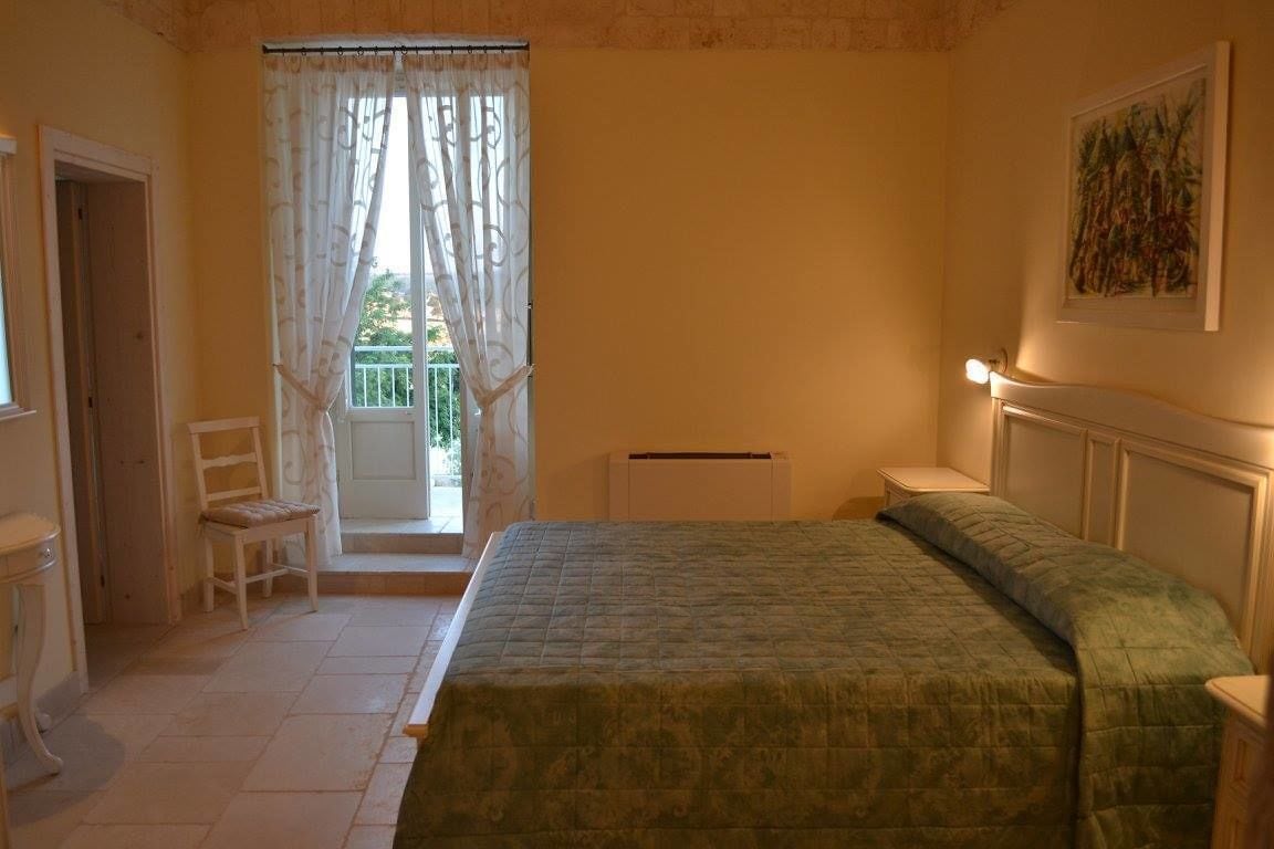 A bedroom with a bed, a chair, a radiator, and a window with curtains.