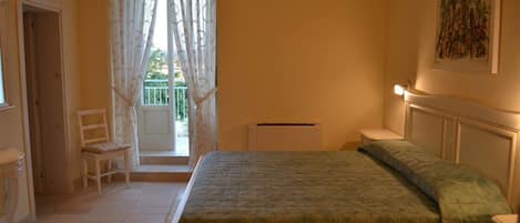 A bedroom with a bed, a chair, a radiator, and a window with curtains.